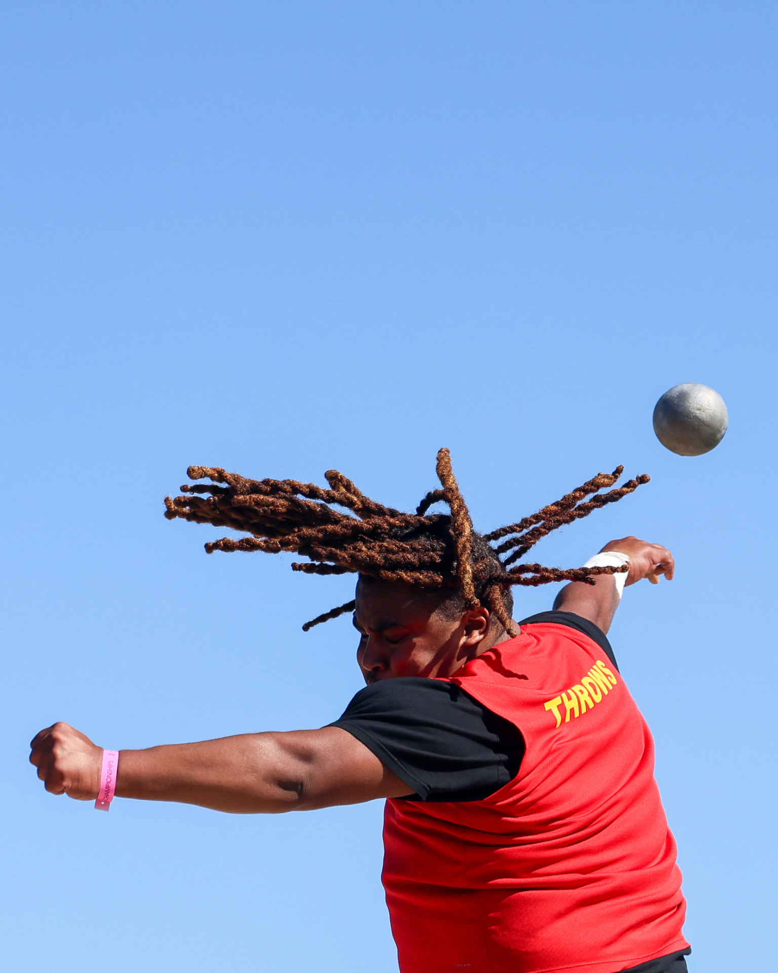 Shot put athlete releasing the shot against a blue sky